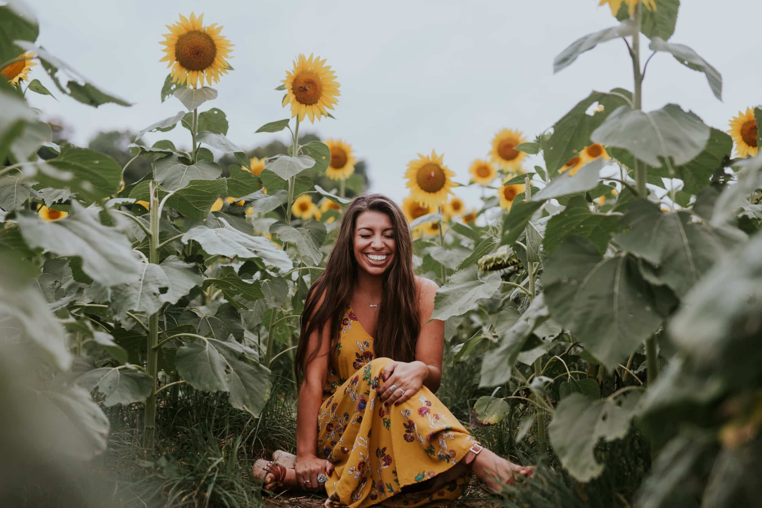 Smiling woman sitting in a sunflower field - Periodontist Southern Pines & Sanford NC | Van Scoyoc Periodontics & Implants Smiling woman sitting in a sunflower field