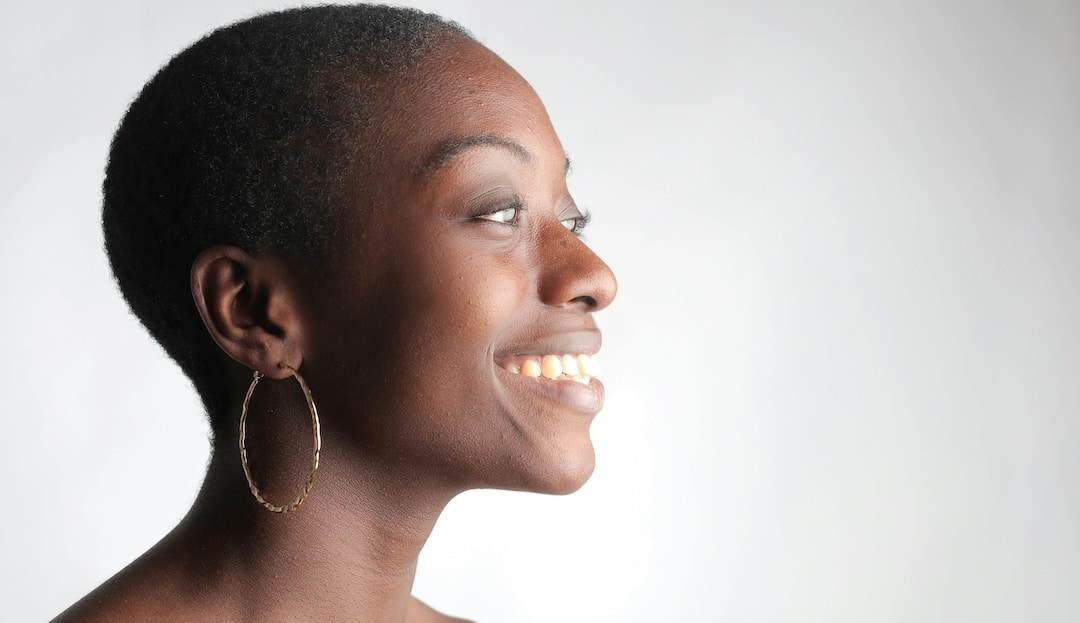 Smiling Black woman in profile with a gold hoop earring against a light background (right-facing side view)